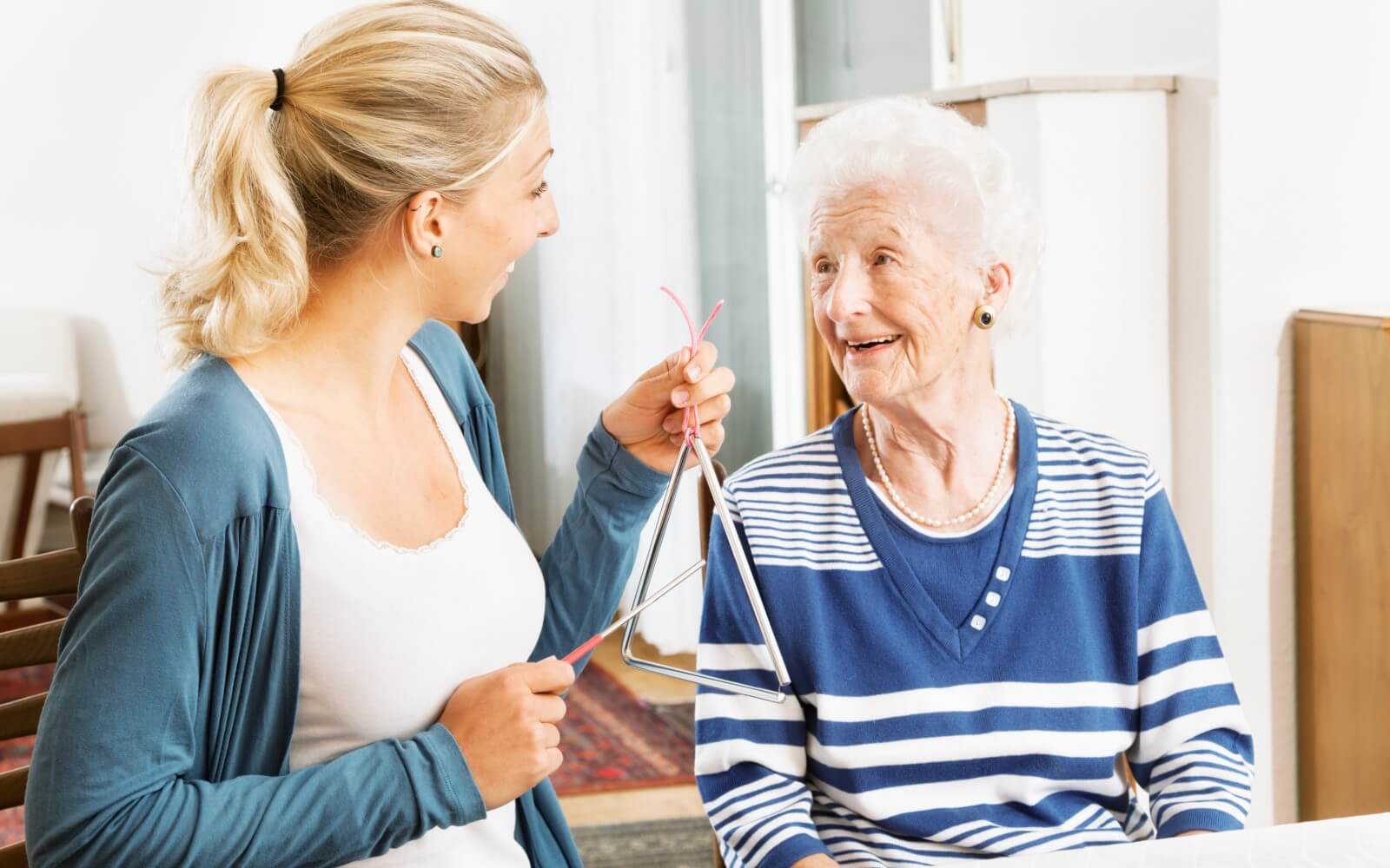 Pflegekraft mit Triangel bei Musiktherapie mit dementer, alter Frau.