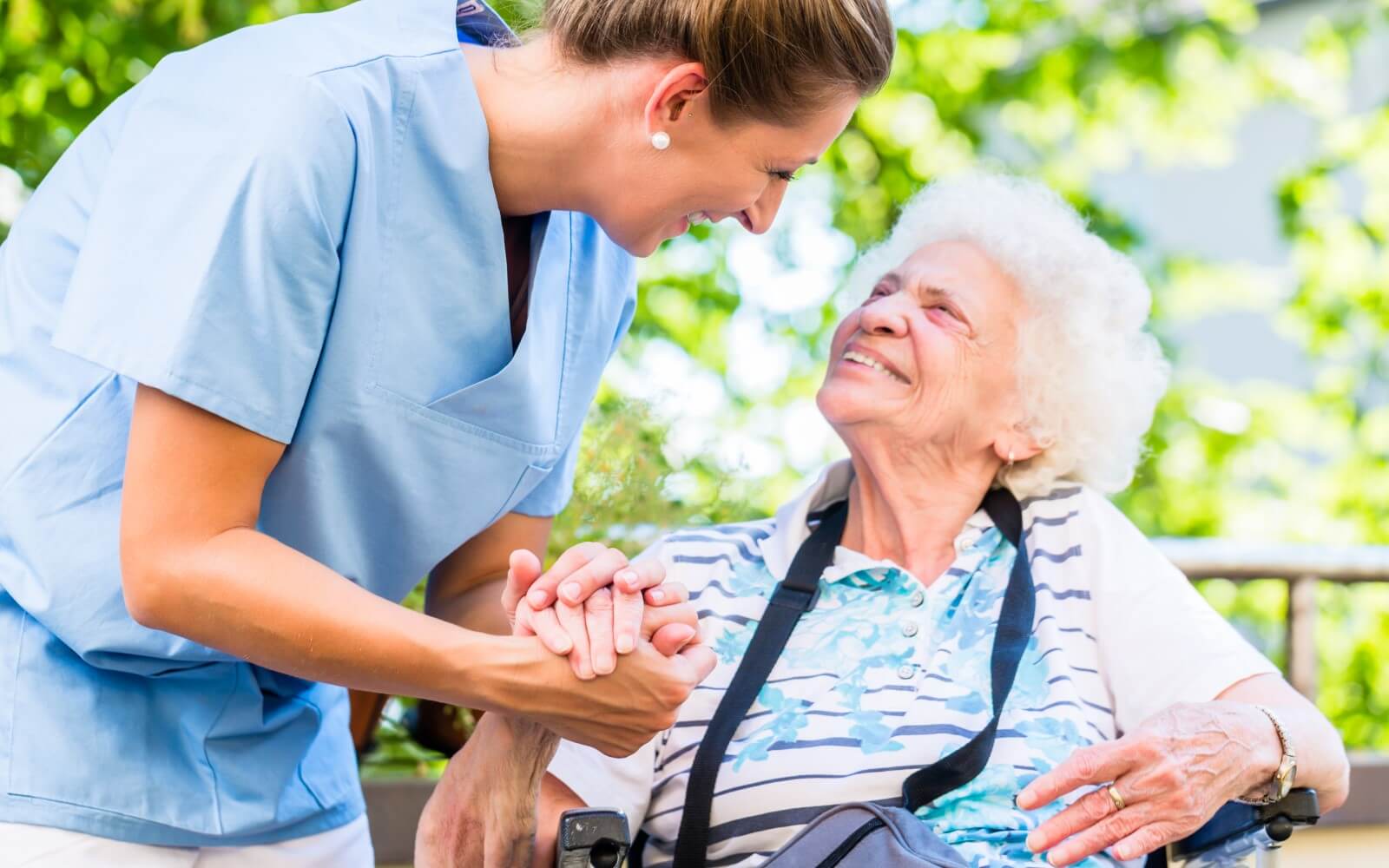 Pflegekraft hält die Hand einer alten Frau beim Gespräch im freien.